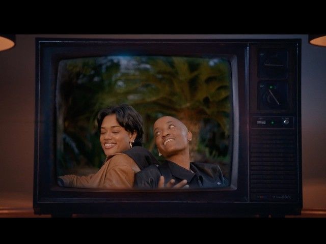 Two people smiling on a TV screen, with a dark retro television frame around them.