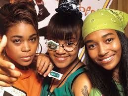 Three friends posing closely together, smiling at the camera, one wearing glasses and a green bandana.