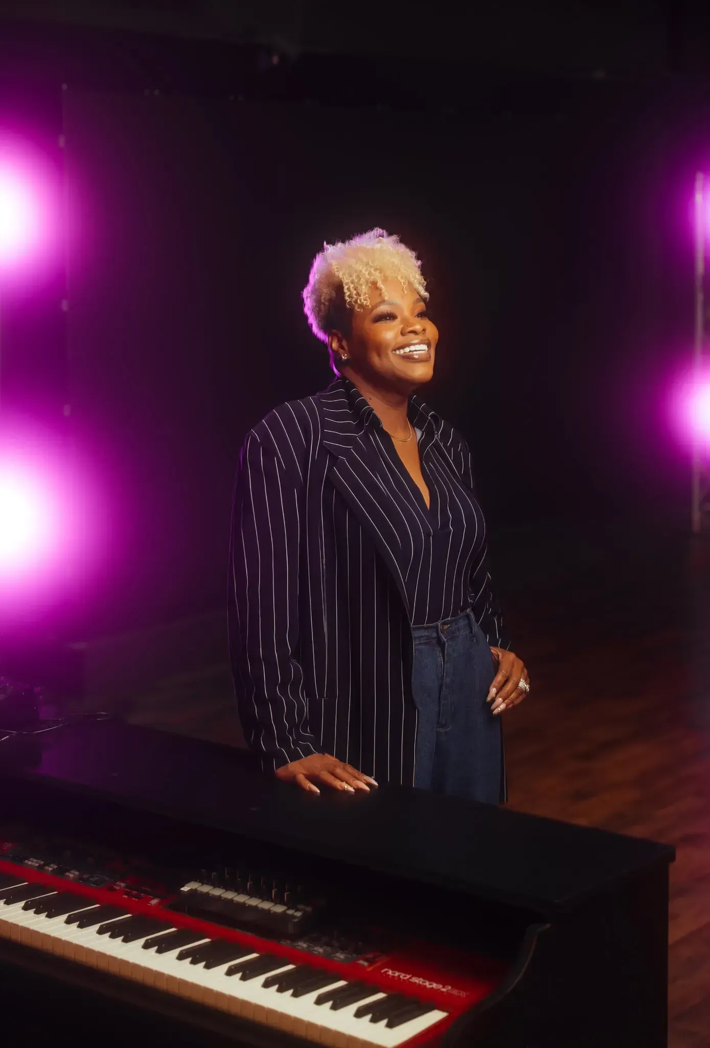 Singer standing by a keyboard on a dark stage with purple lights