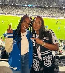 Two fans posing with peace signs at a soccer stadium, wearing blue and black fan gear.