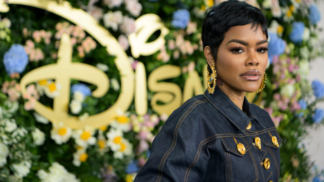 Woman in a dark denim jacket standing before a floral Disney backdrop, looking at the camera.