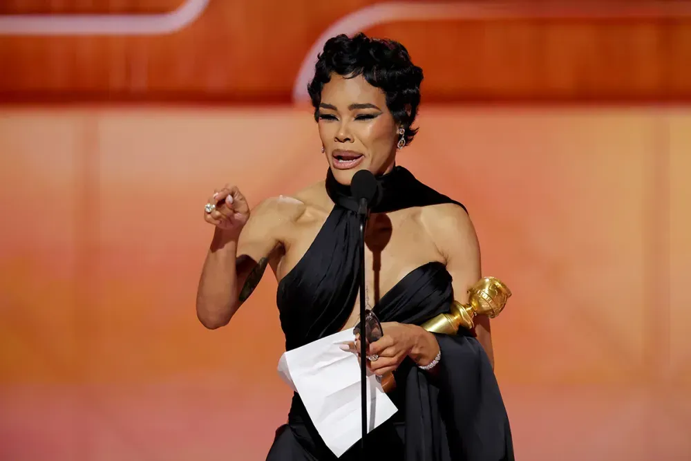 Singer holding a Grammy and speech notes onstage, speaking at a microphone in a black dress