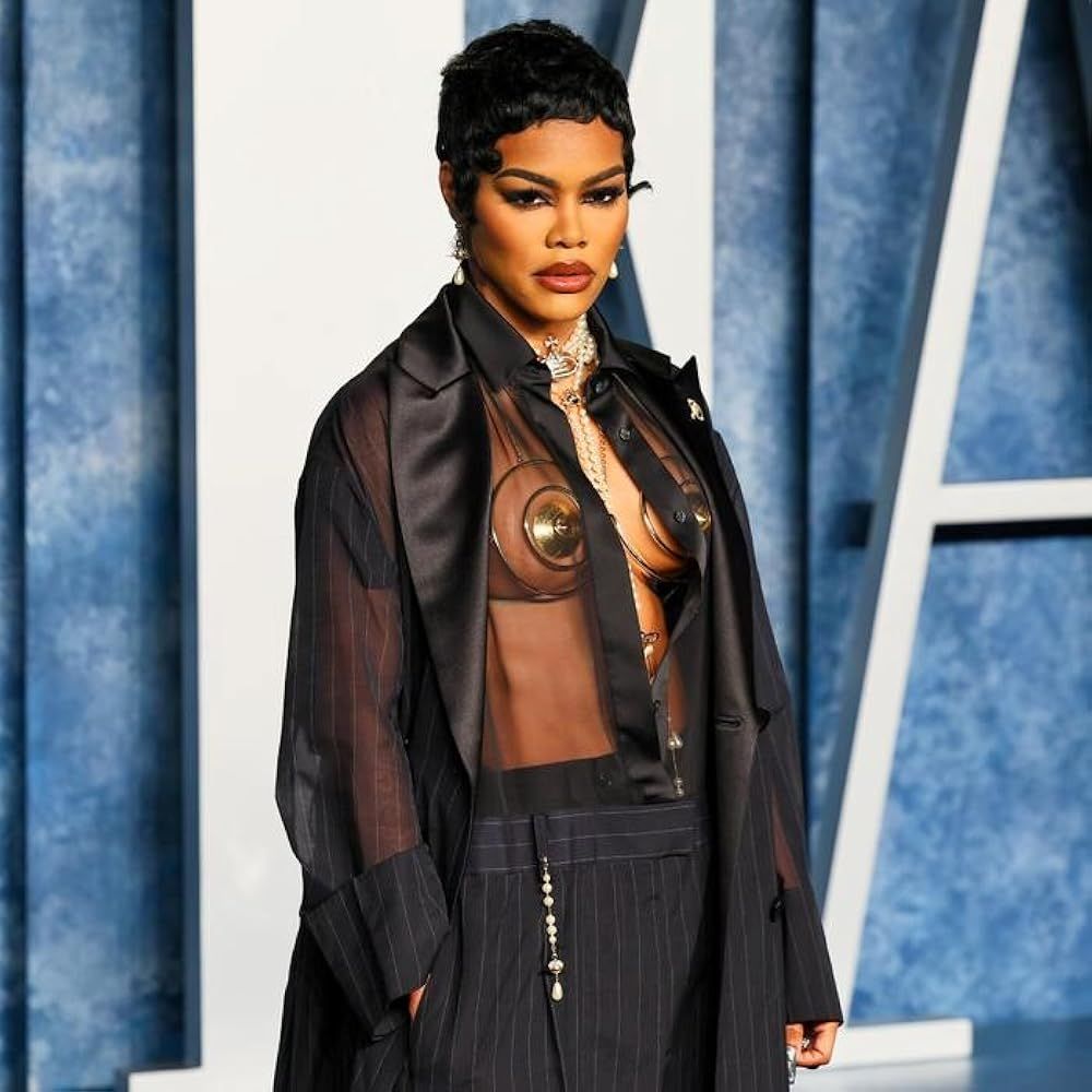 Person in a sheer black outfit posing against a blue patterned backdrop