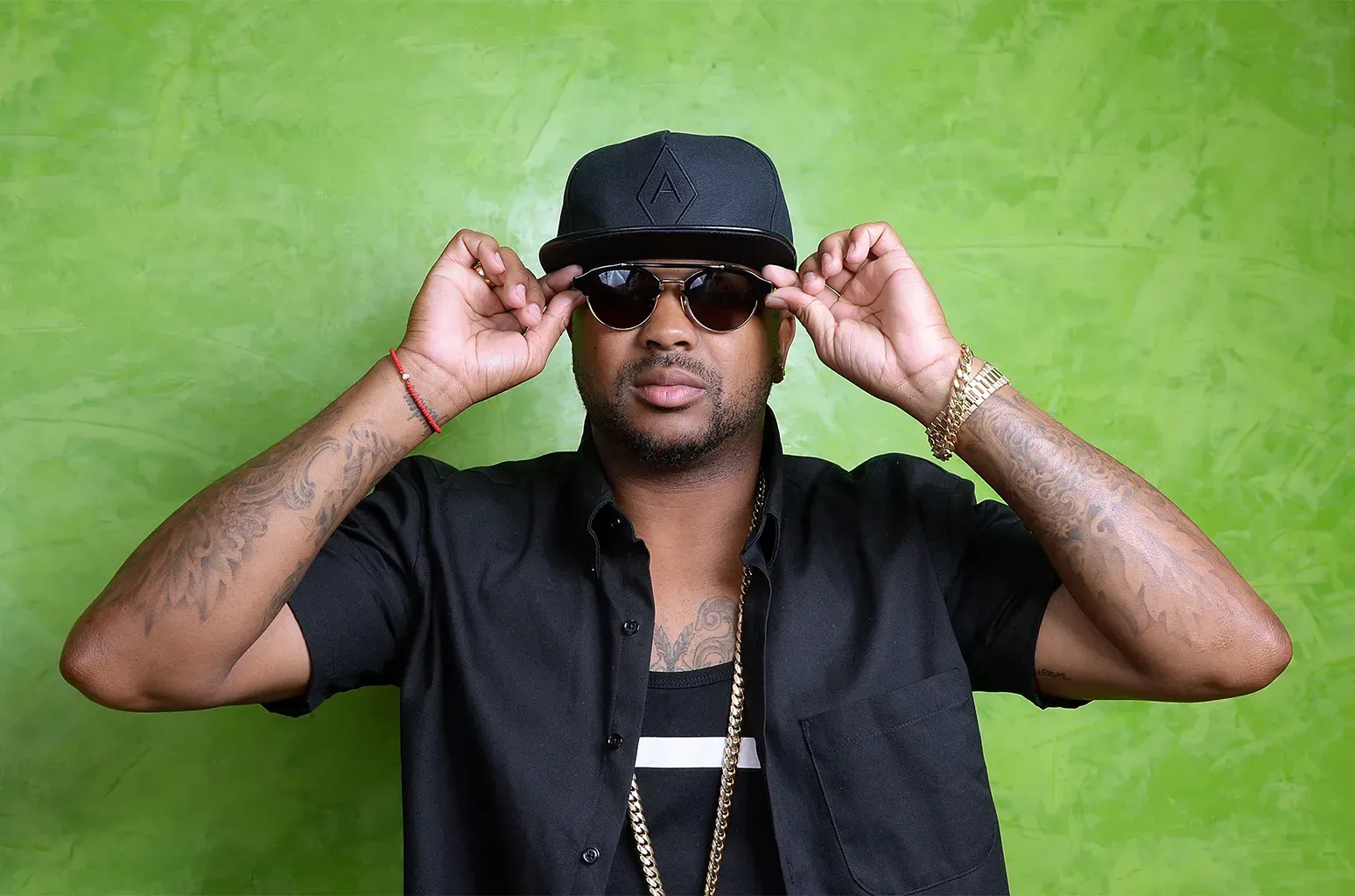 Man in black hat and sunglasses adjusting them against a bright green background