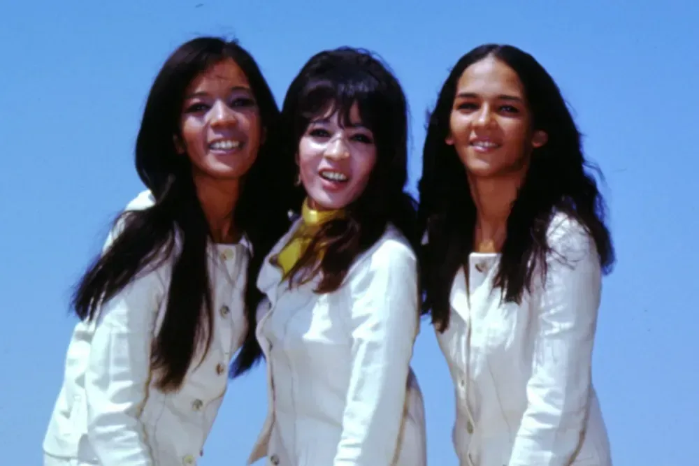 Three people in white clothing smiling against a blue sky backdrop.