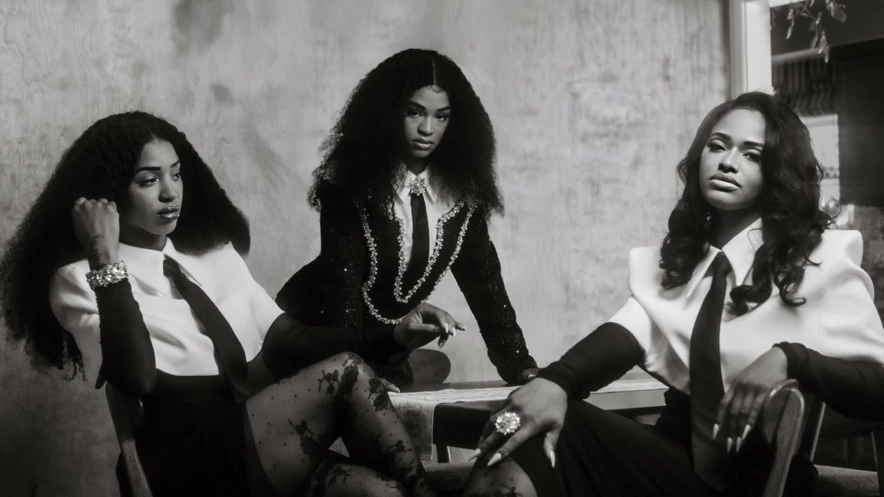 Three people pose in black-and-white, seated on chairs in a studio setting.