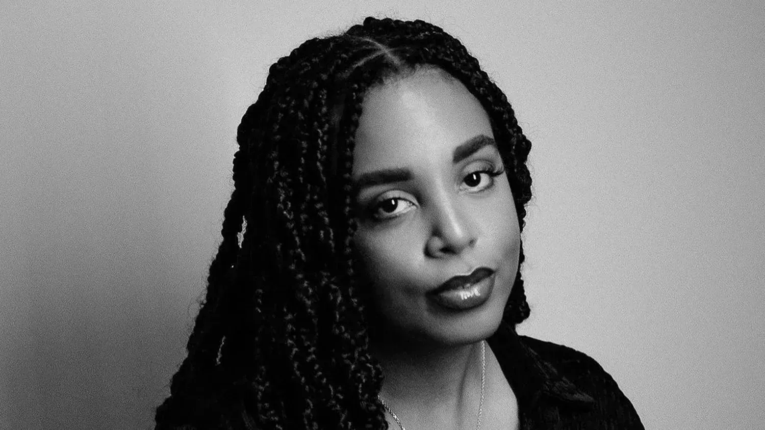 Portrait of a woman with braided hair, looking at the camera against a plain background