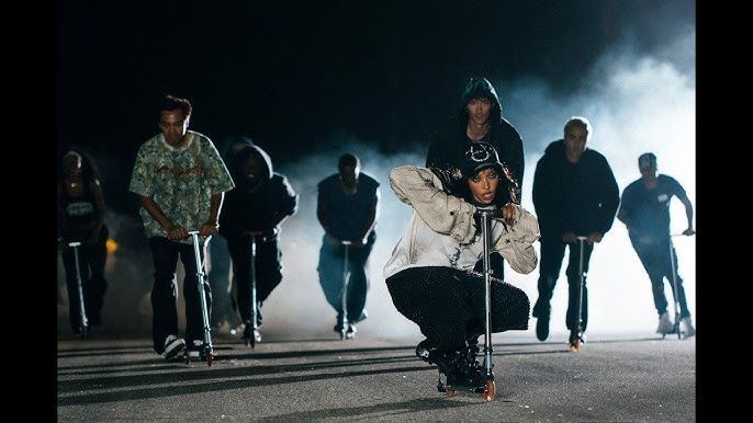 Group of people walking toward the camera at night, with one person crouching in the foreground under bright lights.