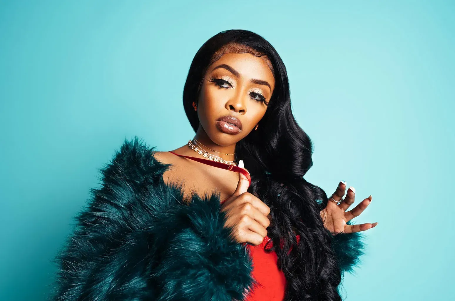 Woman in a teal fur coat and red dress posing against a blue background