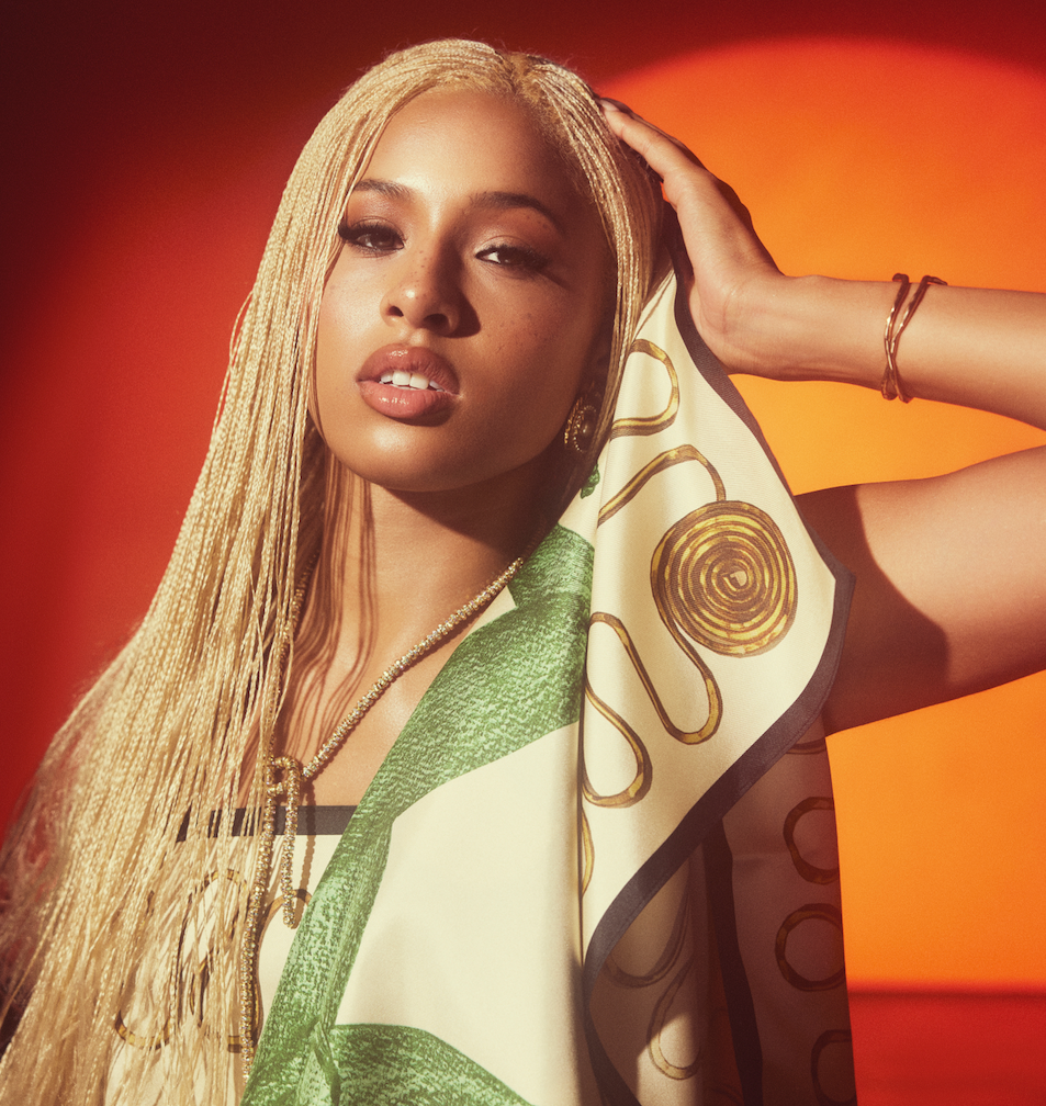 Portrait of a person with braided hair and patterned scarf against a warm orange background