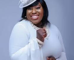Smiling woman in a white outfit and hat against a light gray background.