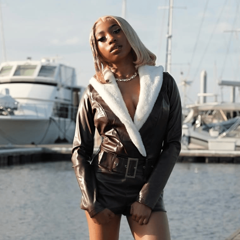 Person in a black shearling jacket standing by yachts at a marina.