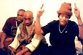 Three people posing indoors, with two seated in front and one in back, hands raised.