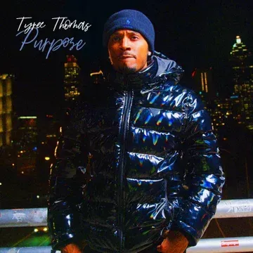 Man in a shiny black jacket and beanie stands at night with city lights behind him, text reads “Type Thomas Purpose”