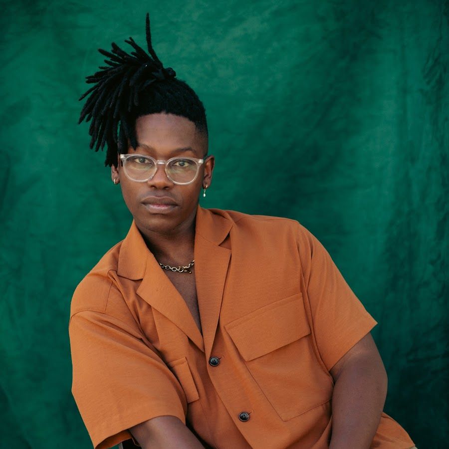 Person in an orange shirt and glasses posing against a green backdrop.