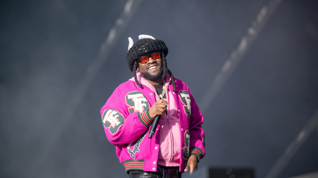 Performer in a bright pink jacket and black beanie singing into a microphone on stage