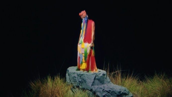 Colorful robed figure standing on a rock in a dark field at night