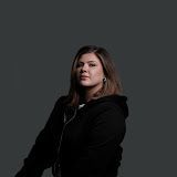 Person with shoulder-length hair in a black hoodie against a dark gray background