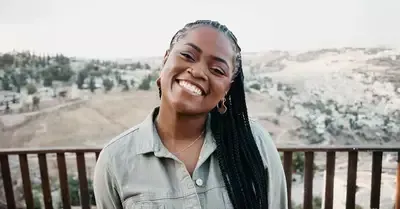 Smiling woman standing on a deck with a blurred hillside landscape in the background