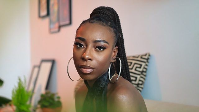 Woman with hoop earrings seated indoors, looking at the camera against a soft, warm background.