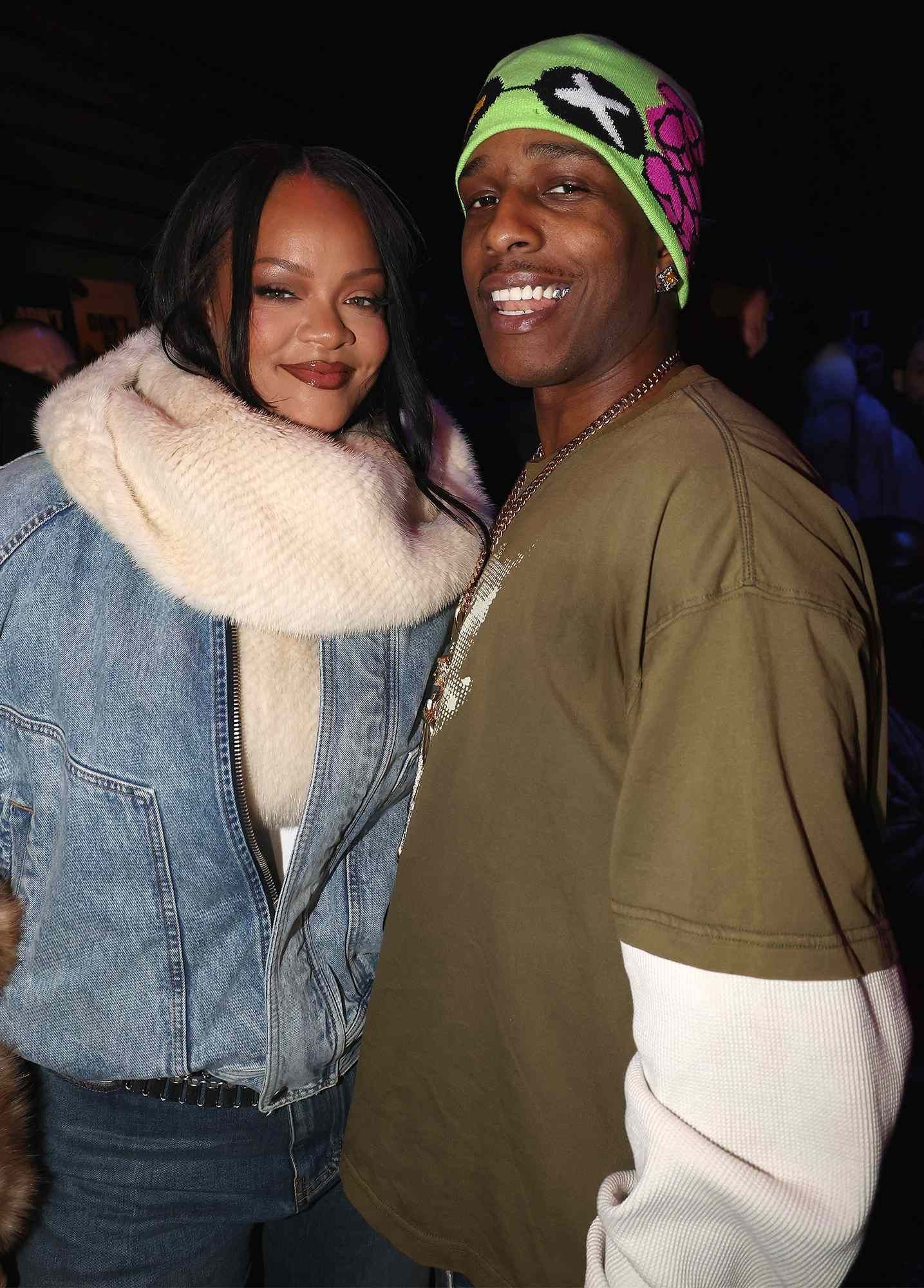 Two people smiling indoors, one in a denim jacket and fur collar, the other in an olive shirt and colorful beanie.