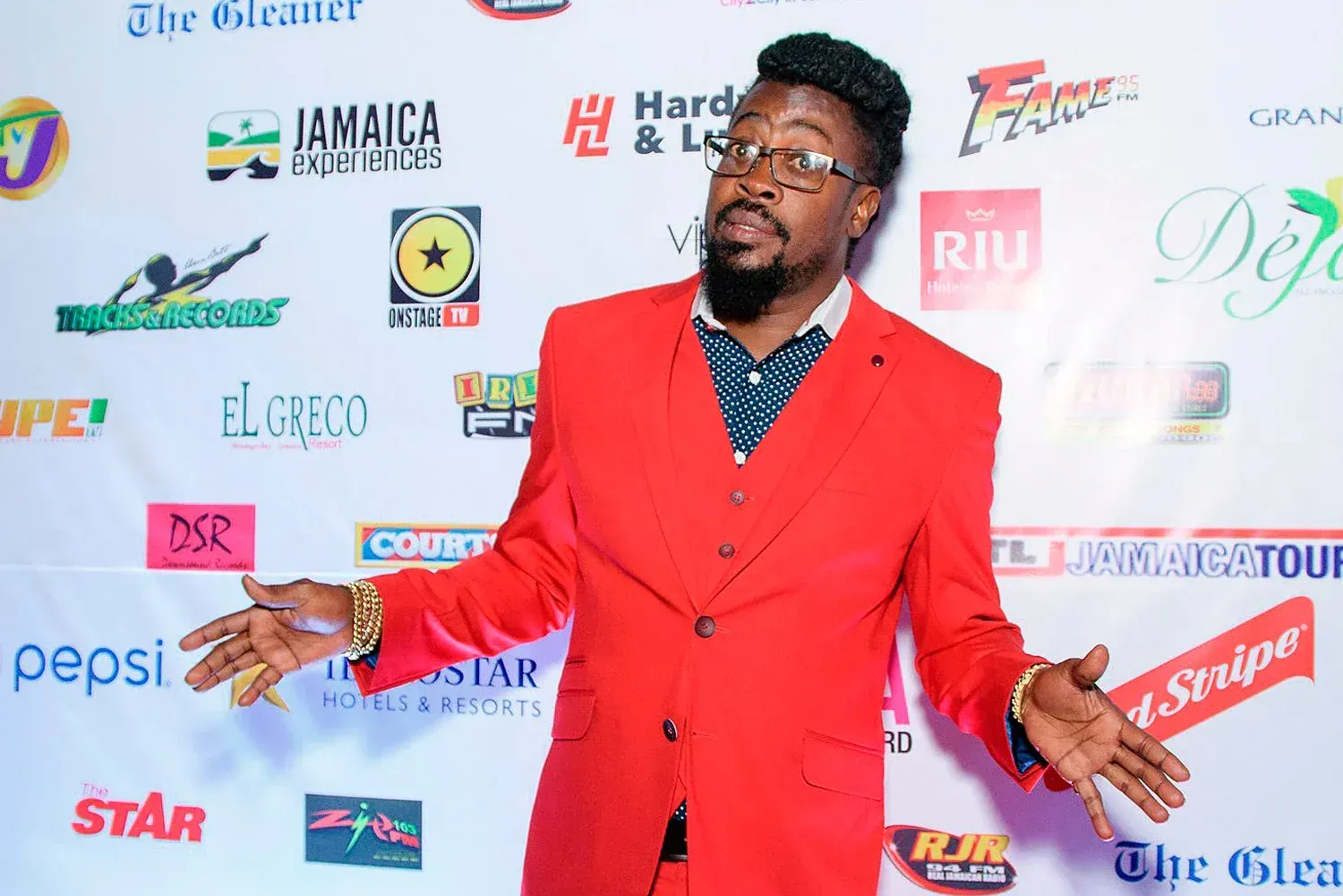 Man in a bright red suit posing on a red carpet before a sponsor backdrop