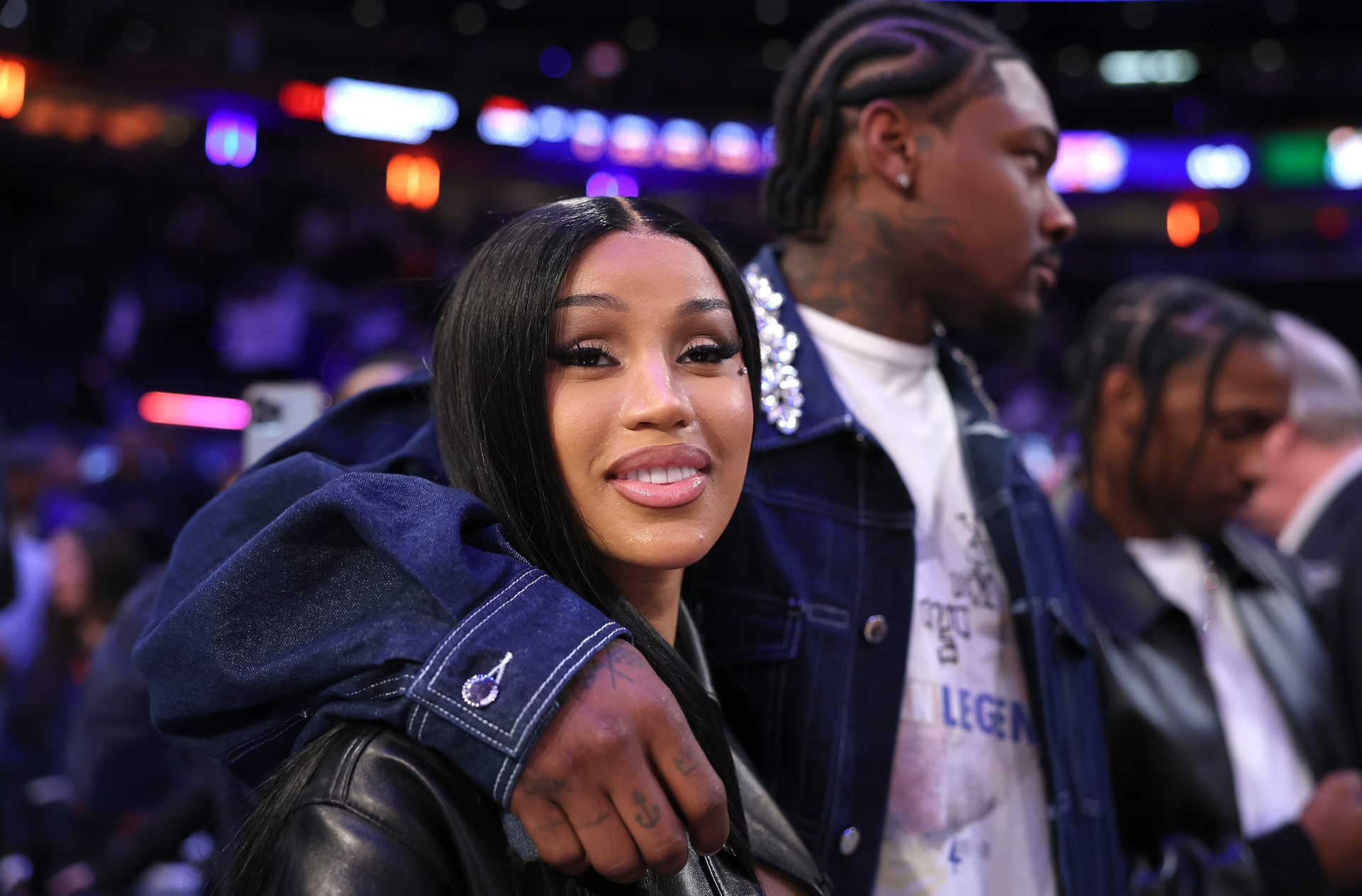 Two smiling people posing courtside, one with an arm around the other, in a brightly lit arena