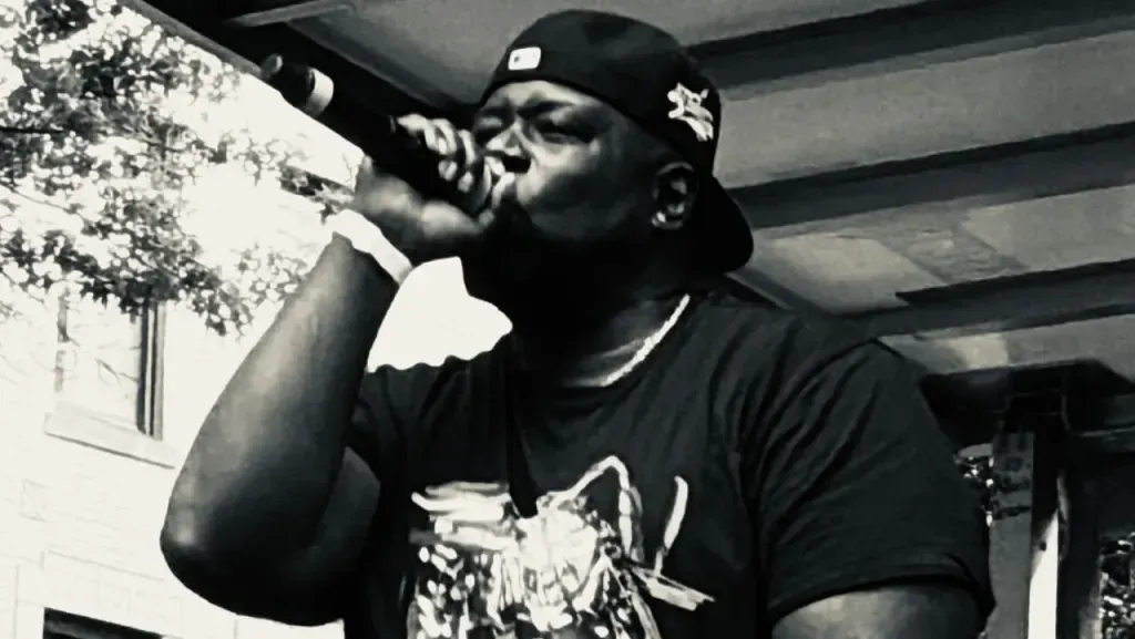 Black-and-white photo of a man singing into a microphone under a covered outdoor area