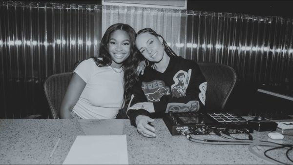 Two people smiling at a table with papers and a turntable in a black-and-white booth setting