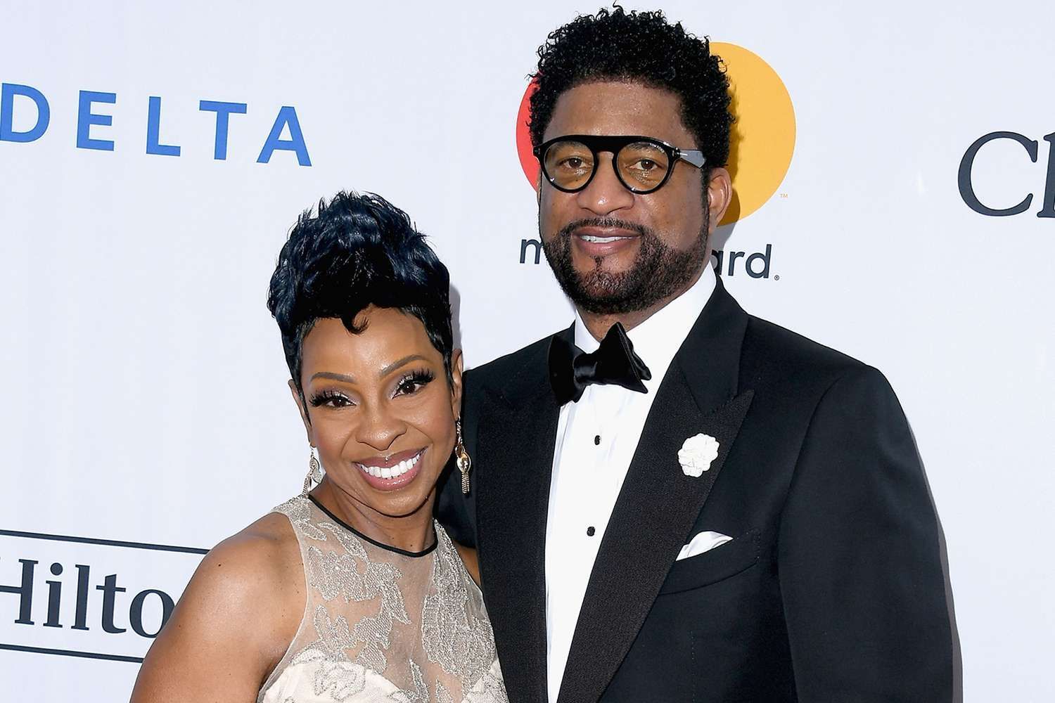 Two people posing on a red carpet in formal attire, smiling before a step-and-repeat backdrop