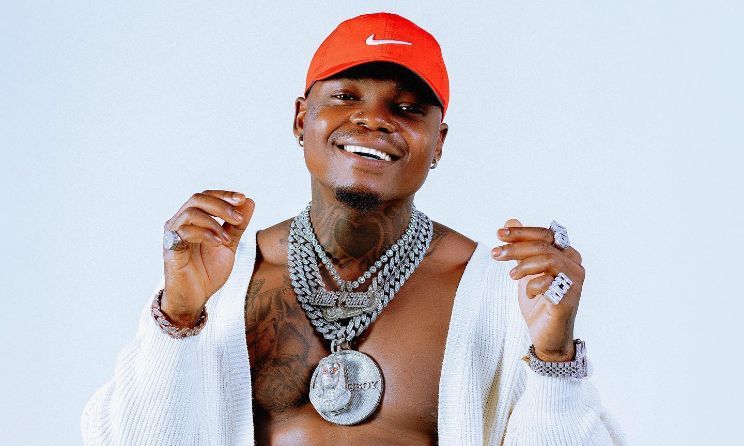 Smiling person in a red cap and white sweater, wearing layered diamond chains against a light background