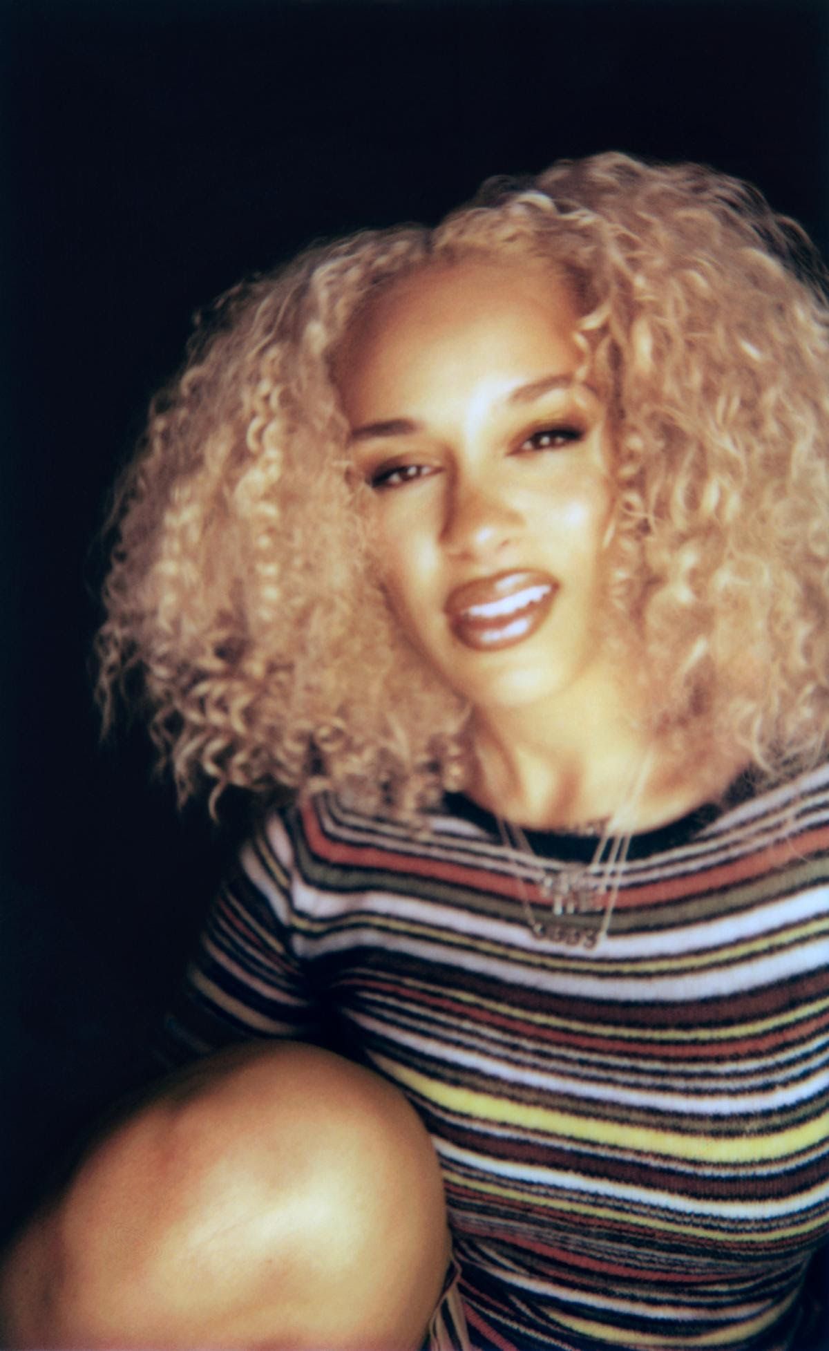 Person with curly blonde hair wearing a striped top against a dark background