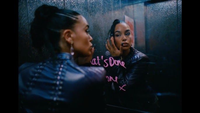 Woman looking in a mirror, writing pink lipstick text on the glass in a dark bathroom.
