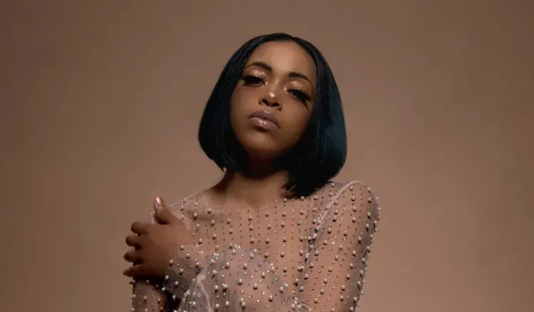 Woman in a beige embellished dress posing against a brown background
