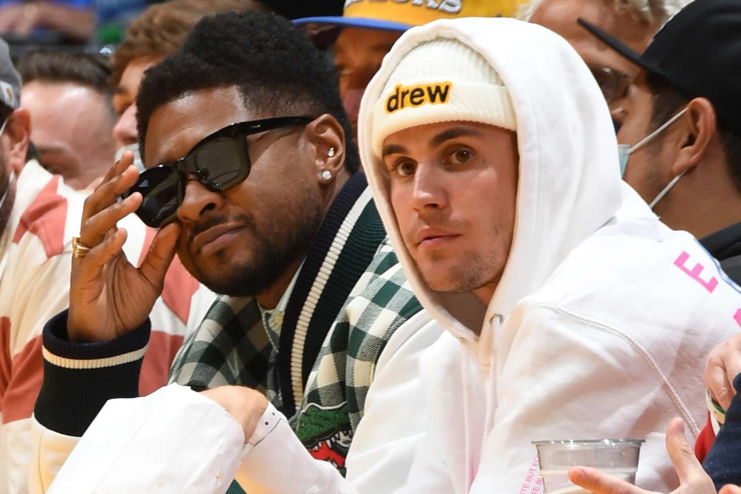 Two men in white hoodies and sunglasses seated at an indoor event, looking toward the camera