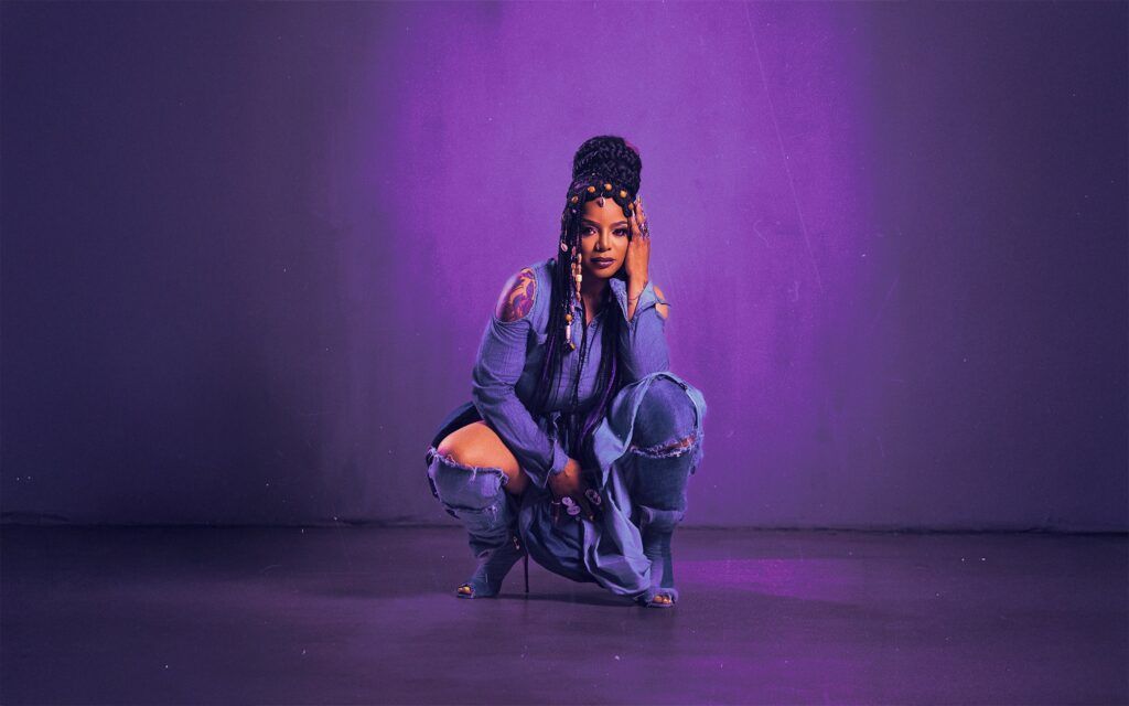 Person crouching on a purple-lit stage in a blue outfit with long braids