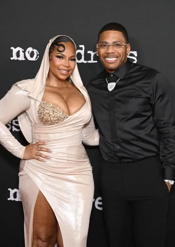Two people posing on a red carpet, smiling in coordinated beige and black formalwear