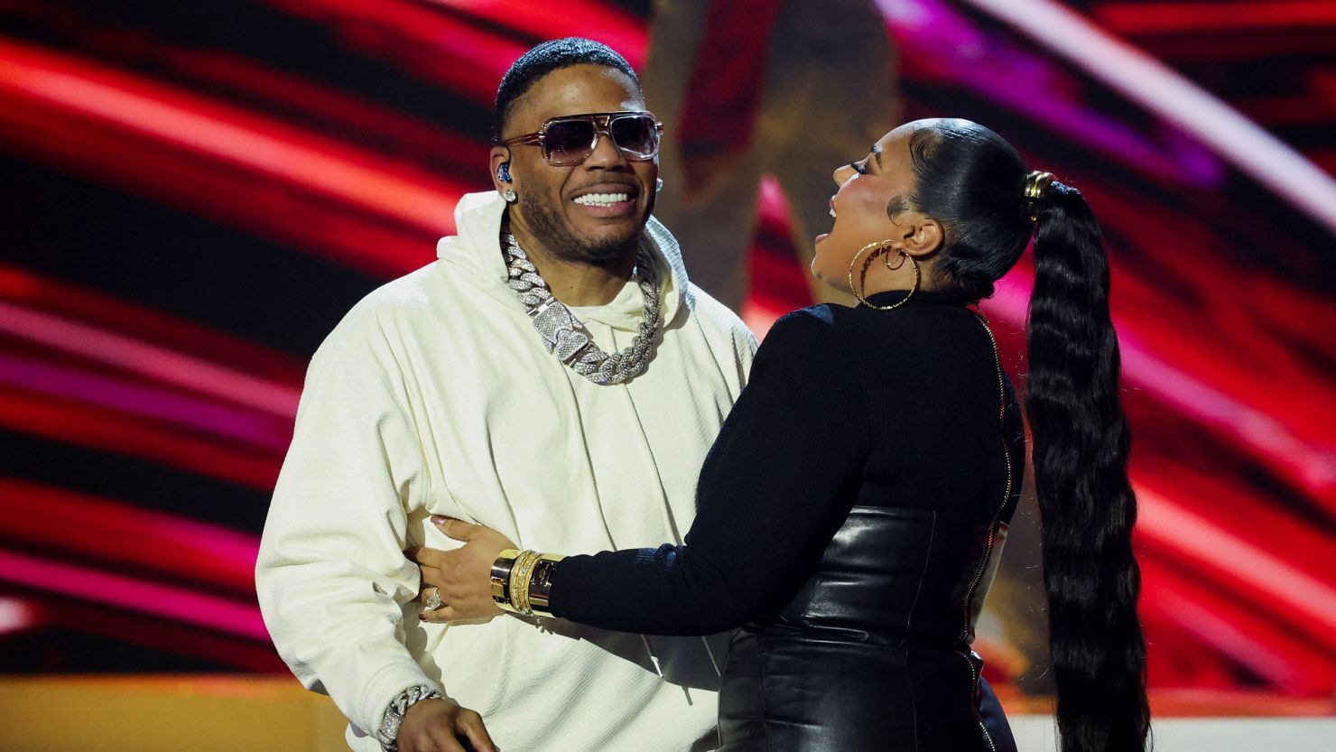 Two people smiling and embracing onstage, with red and pink light streaks in the background