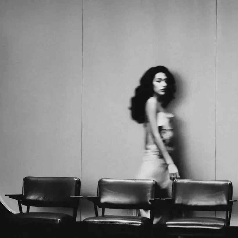 Woman walking past three chairs in a minimalist black-and-white room.