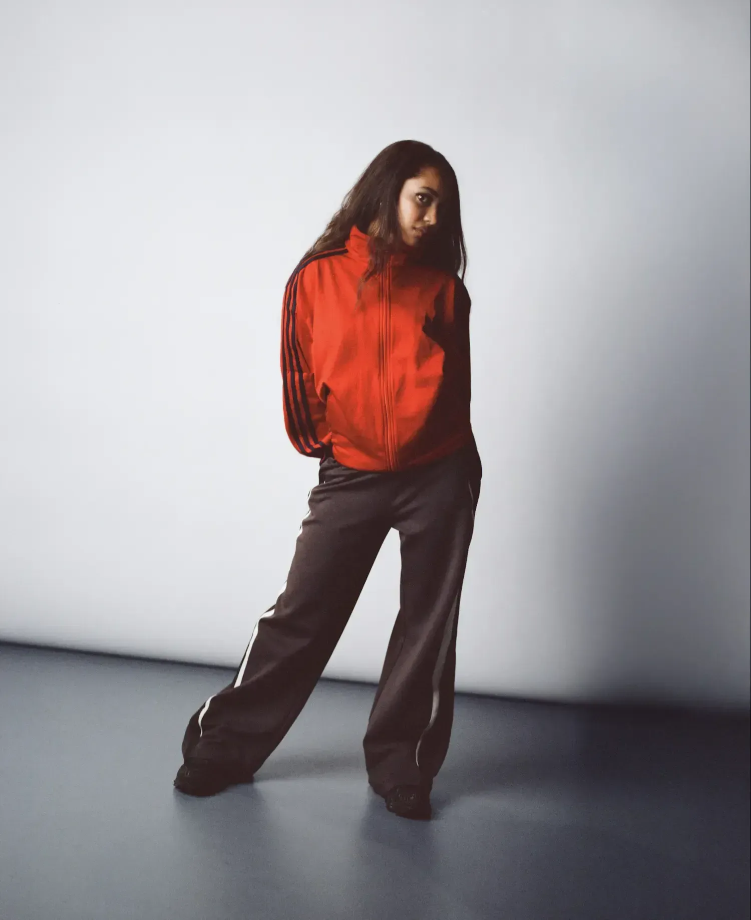 Person in a red jacket and dark pants standing against a plain studio backdrop.