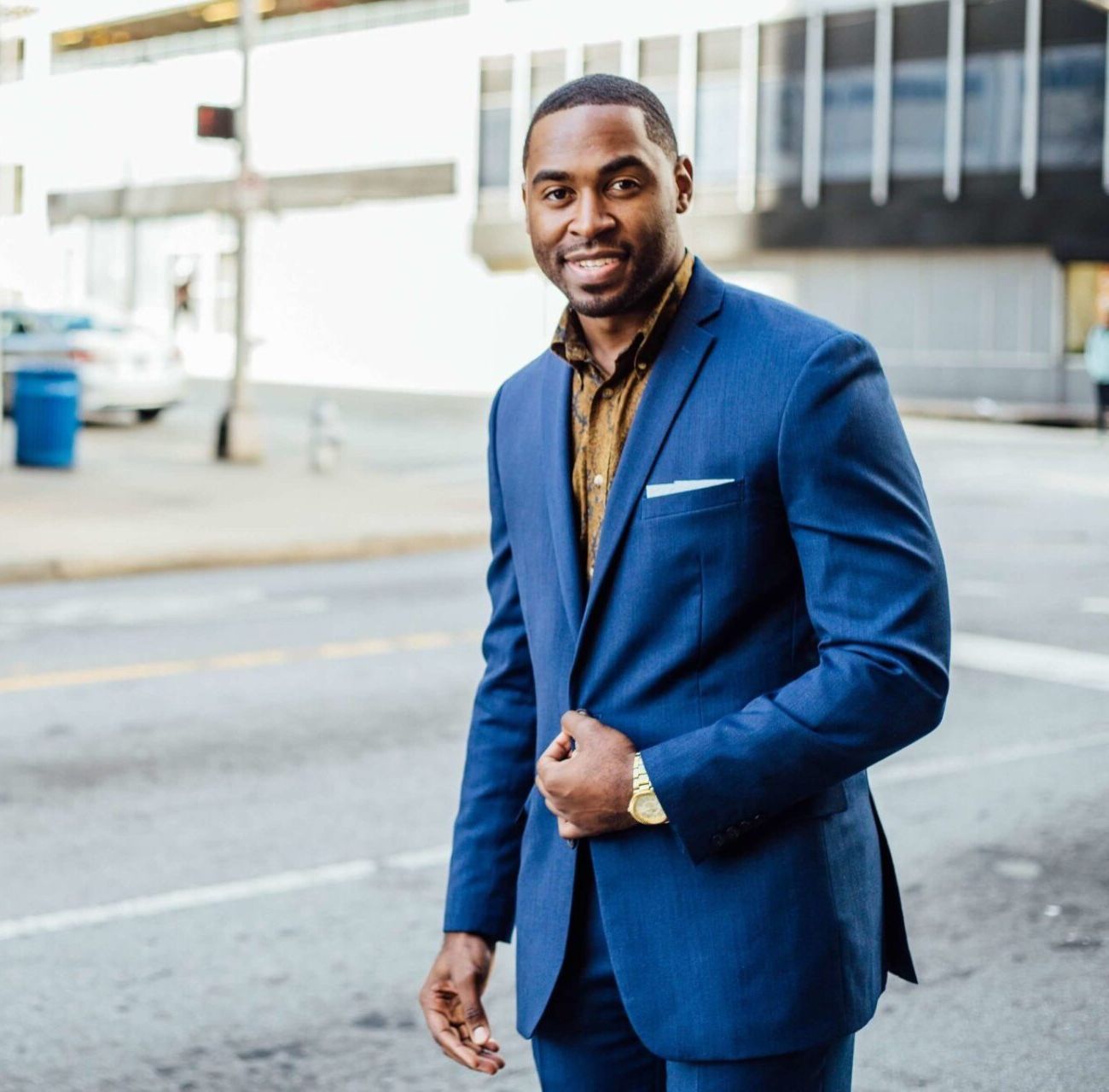 Man in a blue suit smiling on a city street, adjusting his jacket