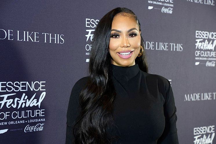 Woman in a black dress smiling on a red carpet at the Essence Festival of Culture backdrop