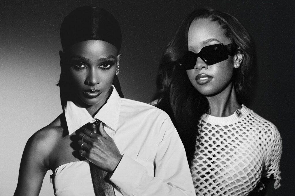Two fashion models pose in black-and-white studio portrait, one in a white shirt and one wearing sunglasses.