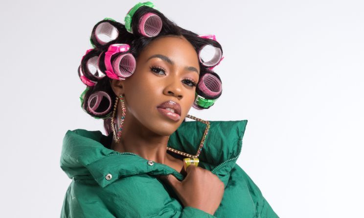 Portrait of a person in a green jacket with pink hair rollers against a light background