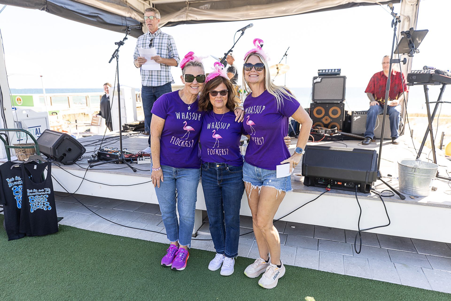 Three people in purple shirts posing onstage with guitars and drums behind them