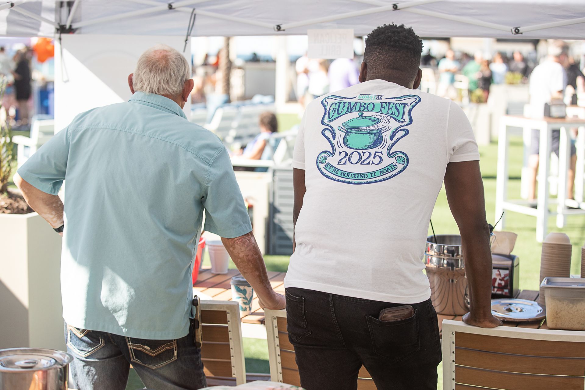 Two people stand under a white canopy outside Coastal for Gumbo Fest