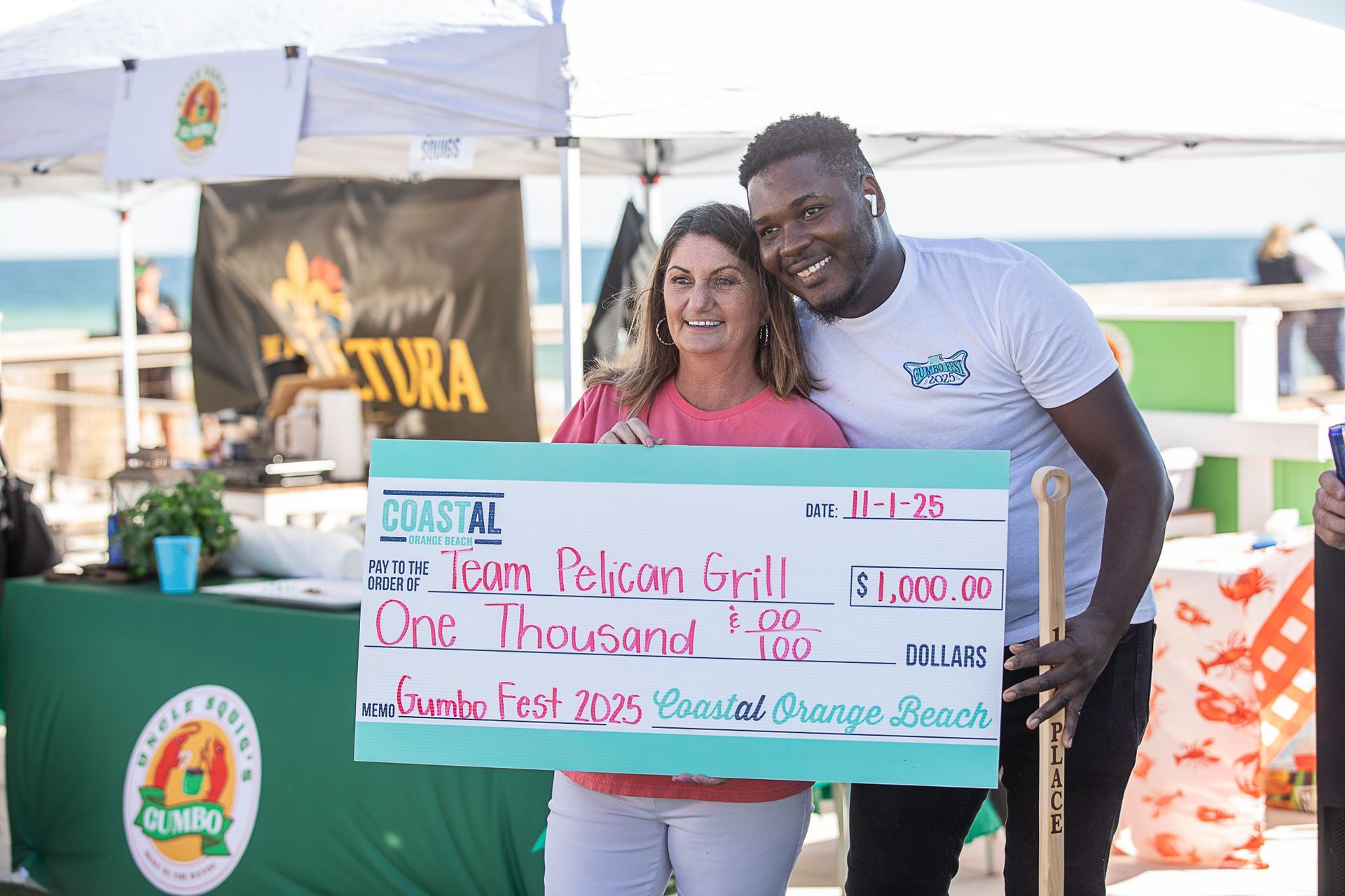 Woman and man posing with a large ceremonial check at an outdoor event booth