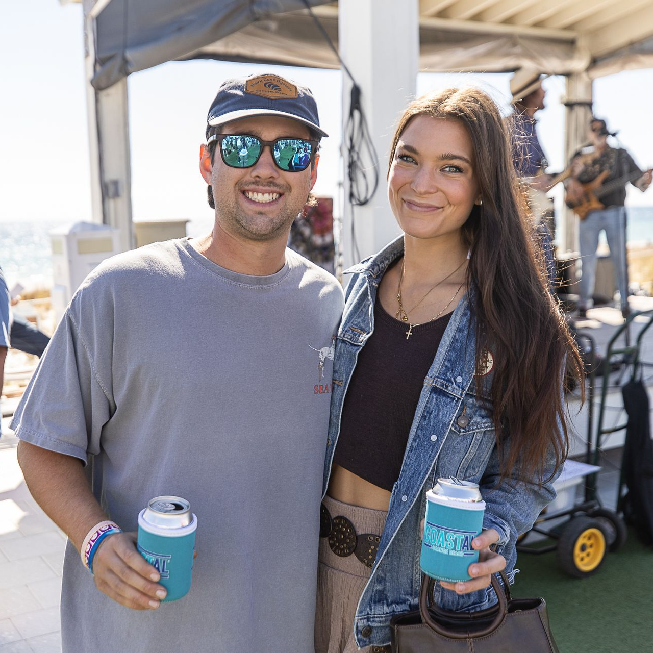 Two people smiling at an outdoor event, holding matching blue cans under a tent.