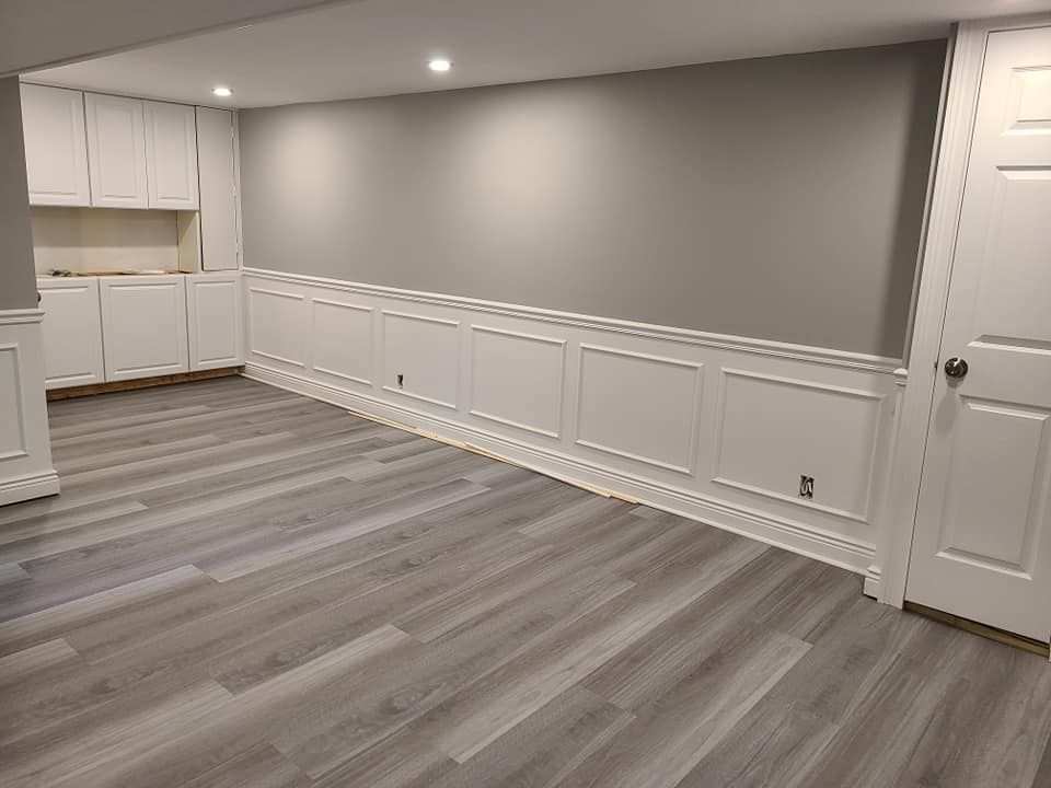 An empty basement with hardwood floors and white cabinets.