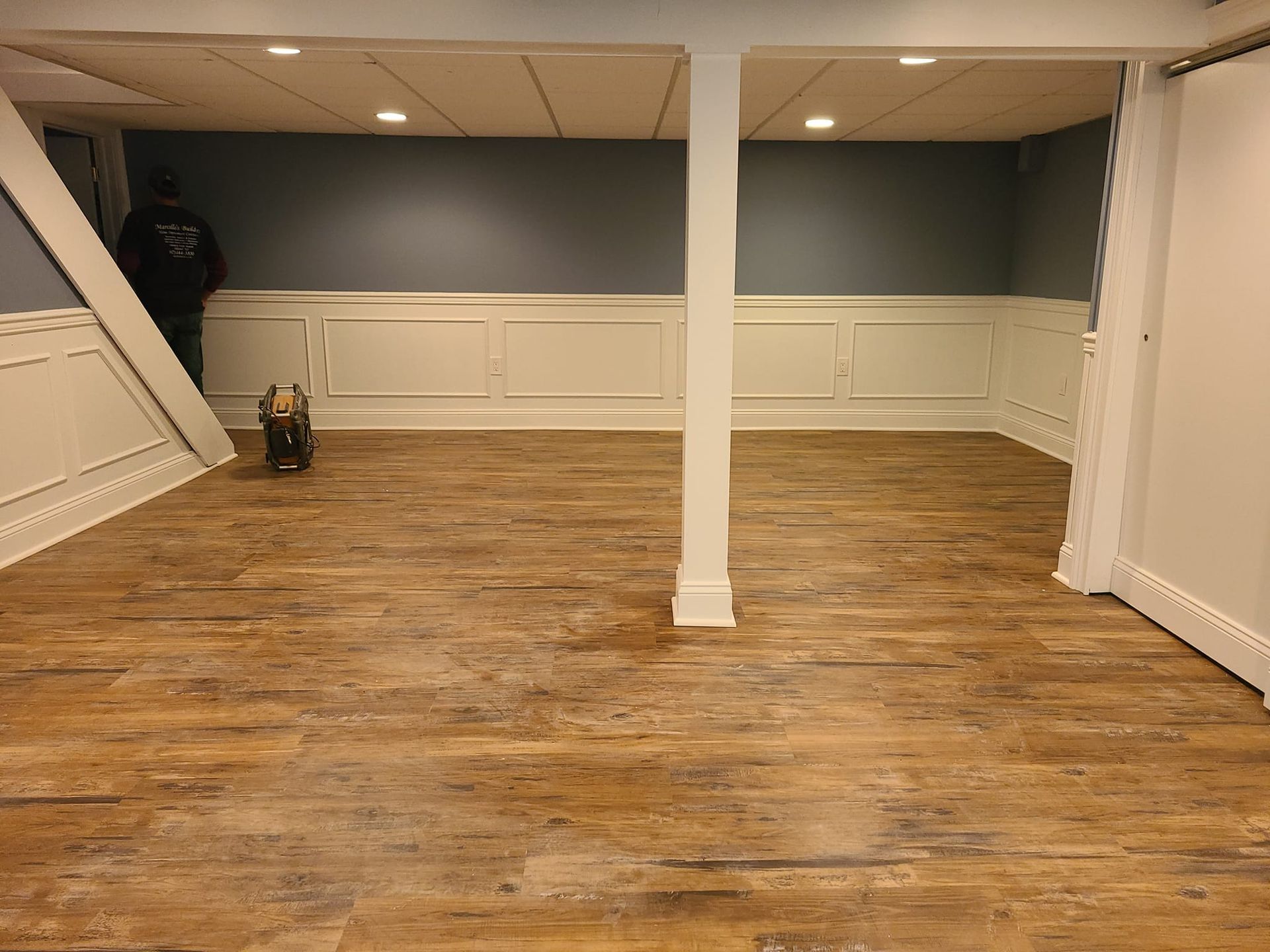 Finished basement with wood-look flooring, white wainscoting, and a blue wall.